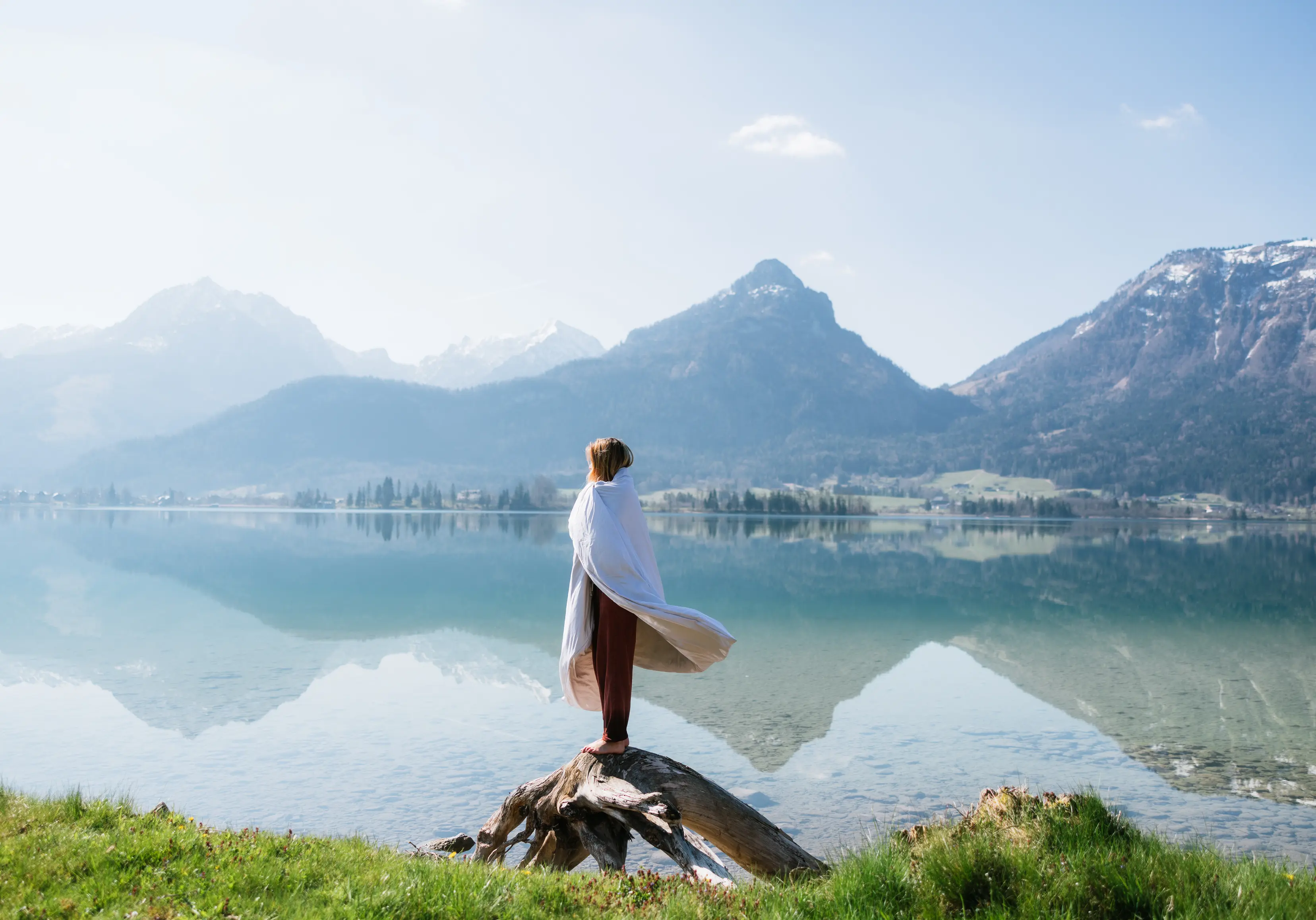 Woman wrapped in a BLACKROLL recovery blanket by an alpine lake.