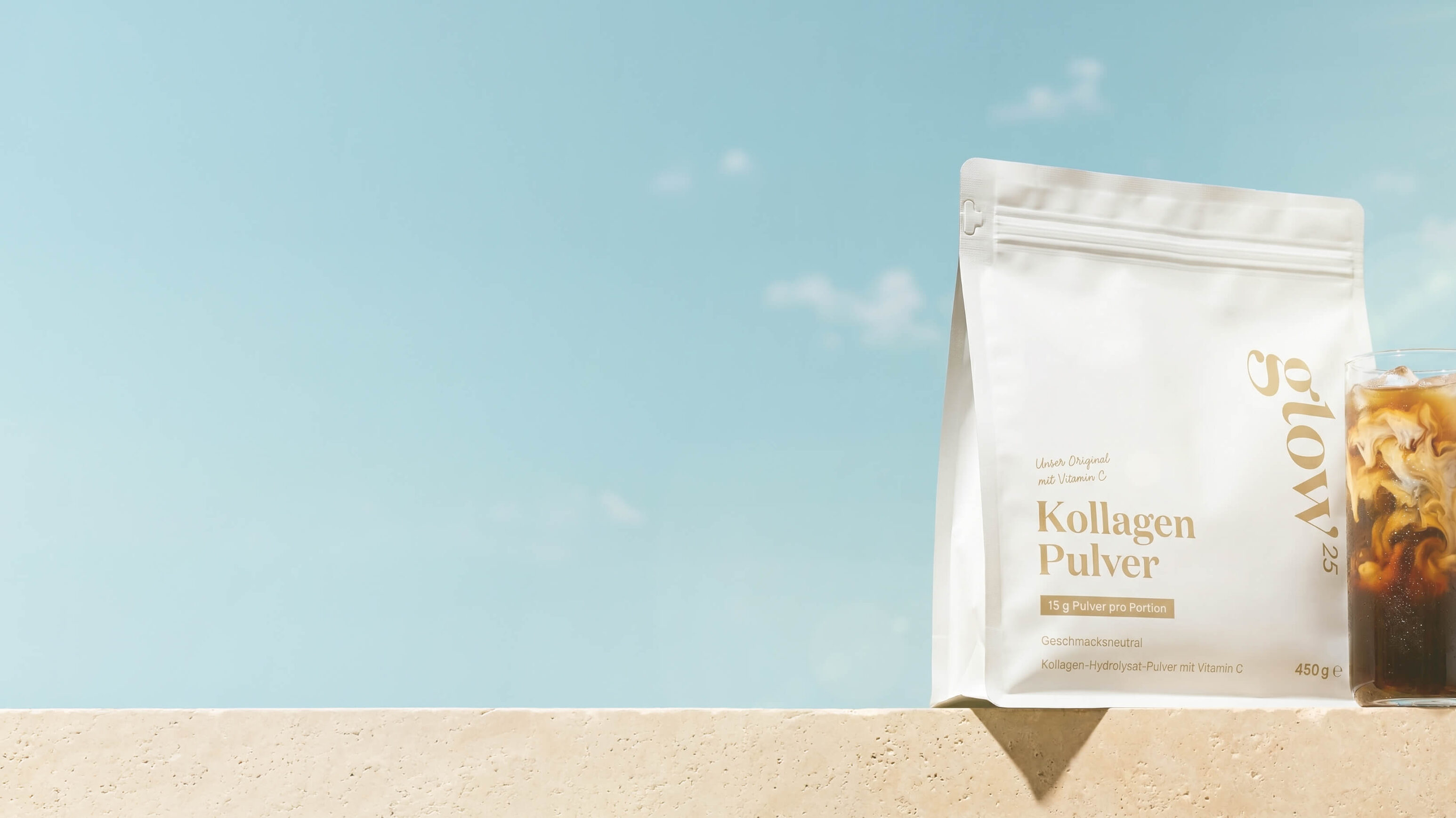 glow25-Kollagenpulver und Eiskaffee auf einer Mauer vor Sommerhimmel.