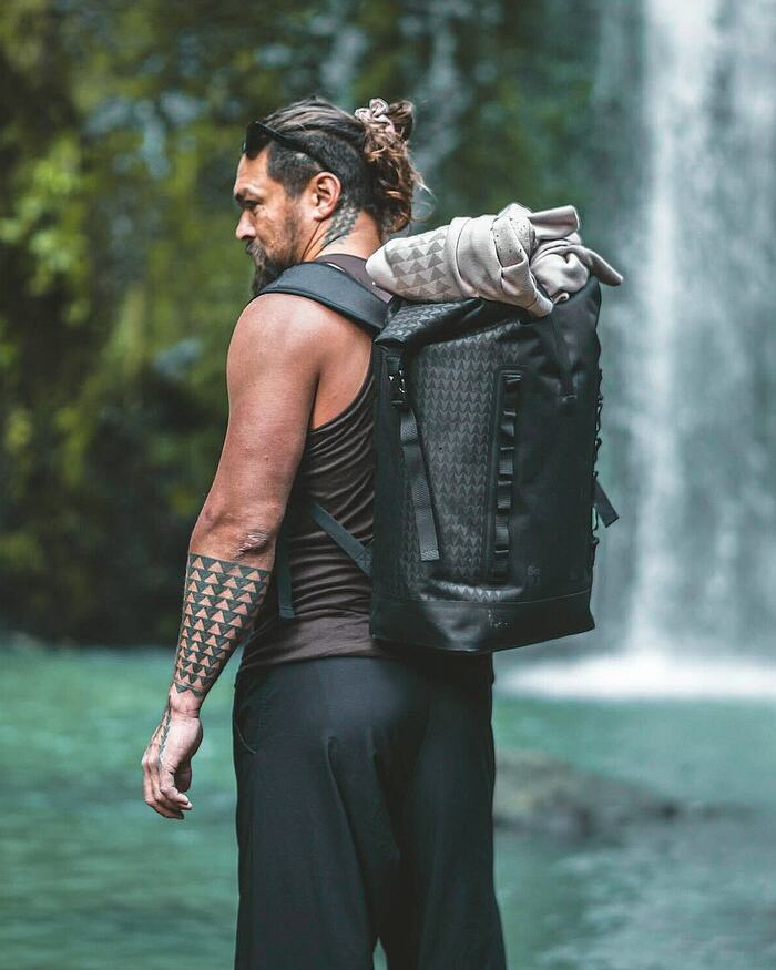 GOT BAG, Mann mit Rucksack steht vor einem Wasserfall im Grünen