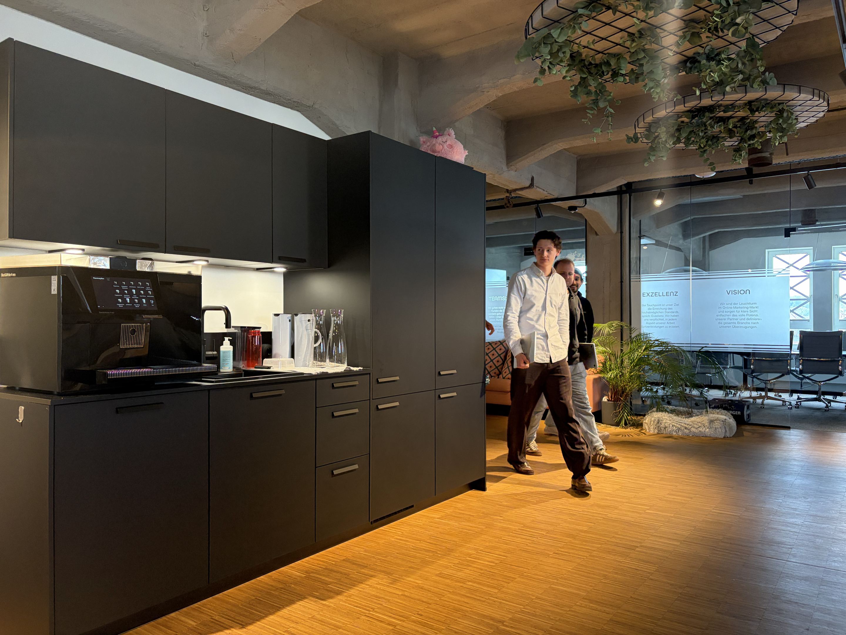 Die Küche im Touchpoint-Büro, dahinter das offene Büro mit Pflanzen und Tageslicht.