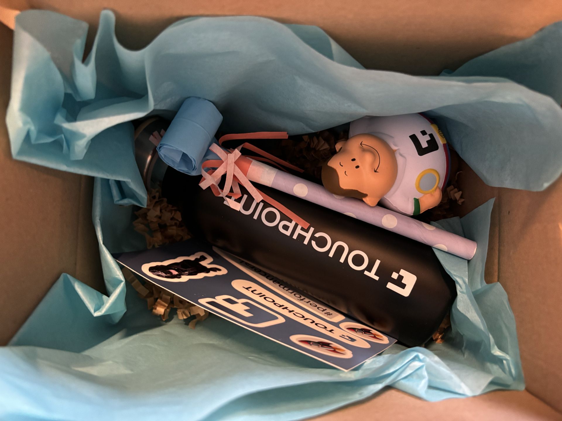 Willkommenspaket im Karton: Touchpoint-Flasche, Notizbuch, Stift und Spardose.
